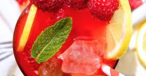 Fizzy Raspberry Lemonade Party Punch garnished with fresh lemons and fresh raspberries in a glass with a straw on a party table