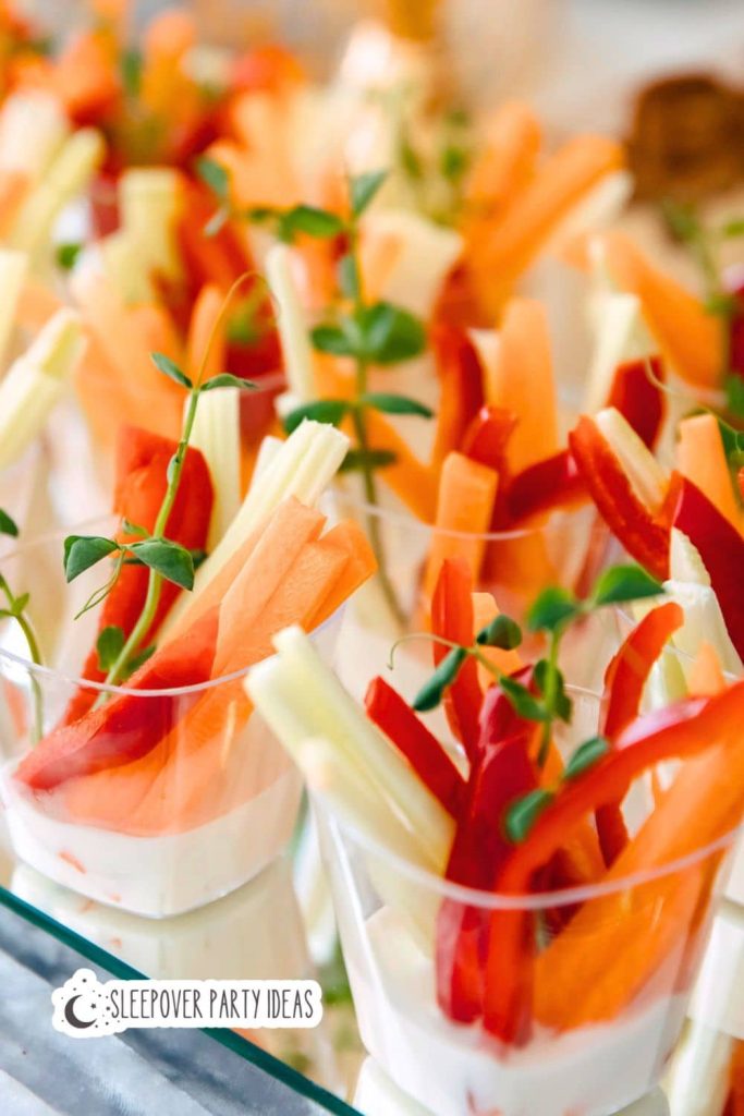 DIY Graduation Party Finger Foods Assorted vegetable sticks including carrots, celery, and red peppers served in small clear cups with a creamy dip for a boho graduation party menu appetizers and finger foods